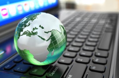 Eine gläserne Weltkugel liegt auf einer Tastaur eines Laptops.