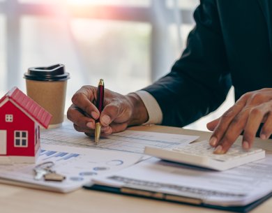 Geschäftsstelle Gutachterausschuss Bild eines Schreibtisches mit Dokumenten zu einem Wertgutachten und einer Person mit Stift sowie Taschenrechner in der Hand.