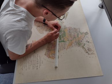 Ein Mitarbeiter des Katasteramtes greift auf einer historischen Karte ein Maß ab.