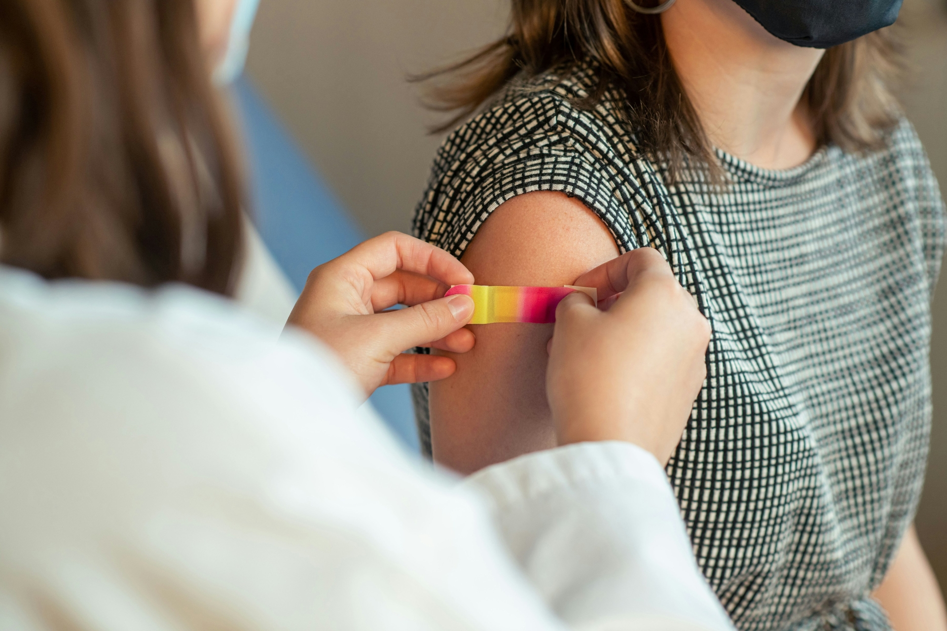 Eine Ärztin klebt ein buntes Pflaster auf den Arm einer Patientin.