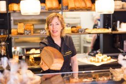 Eine Dame steht in einer Bäckerei hinter einem Verkaufstresen und hält ein Brot in der Hand