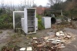 Alter, kaputter Kühlschrank, andere defekte Gerätschaften auf einer betonierten Fläche mit weiteren kaputten Einzelteilen im Vordergrund 
