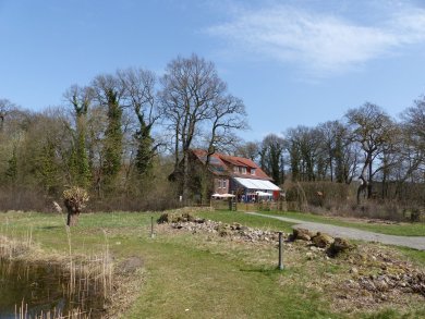 Ansicht Gut Nordholz Seitenansicht auf ein Gebäude des Gut Nordholz, aus dem Garten heraus fotografiert, ein kleiner Teil vom Teich im Vordergrund zu erkennen.