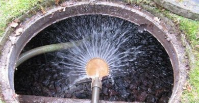 Geöffneter kreisförmiger Einlass in den Boden (Gullideckel), in den mit einem Schlauch Wasser eingeführt wird.