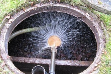 Abwasserbeseitigungsanlage Geöffneter kreisförmiger Einlass in den Boden (Gullideckel), in den mit einem Schlauch Wasser eingeführt wird.