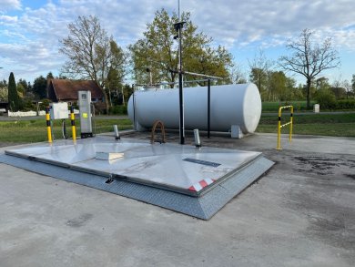 Eigenverbrauchstankstelle Anlage eines Öltanks auf einer betonierten Fläche. Tank im Hintergrund, im Vordergrund Luke im Boden, weitere Gerätschaften neben Öltank