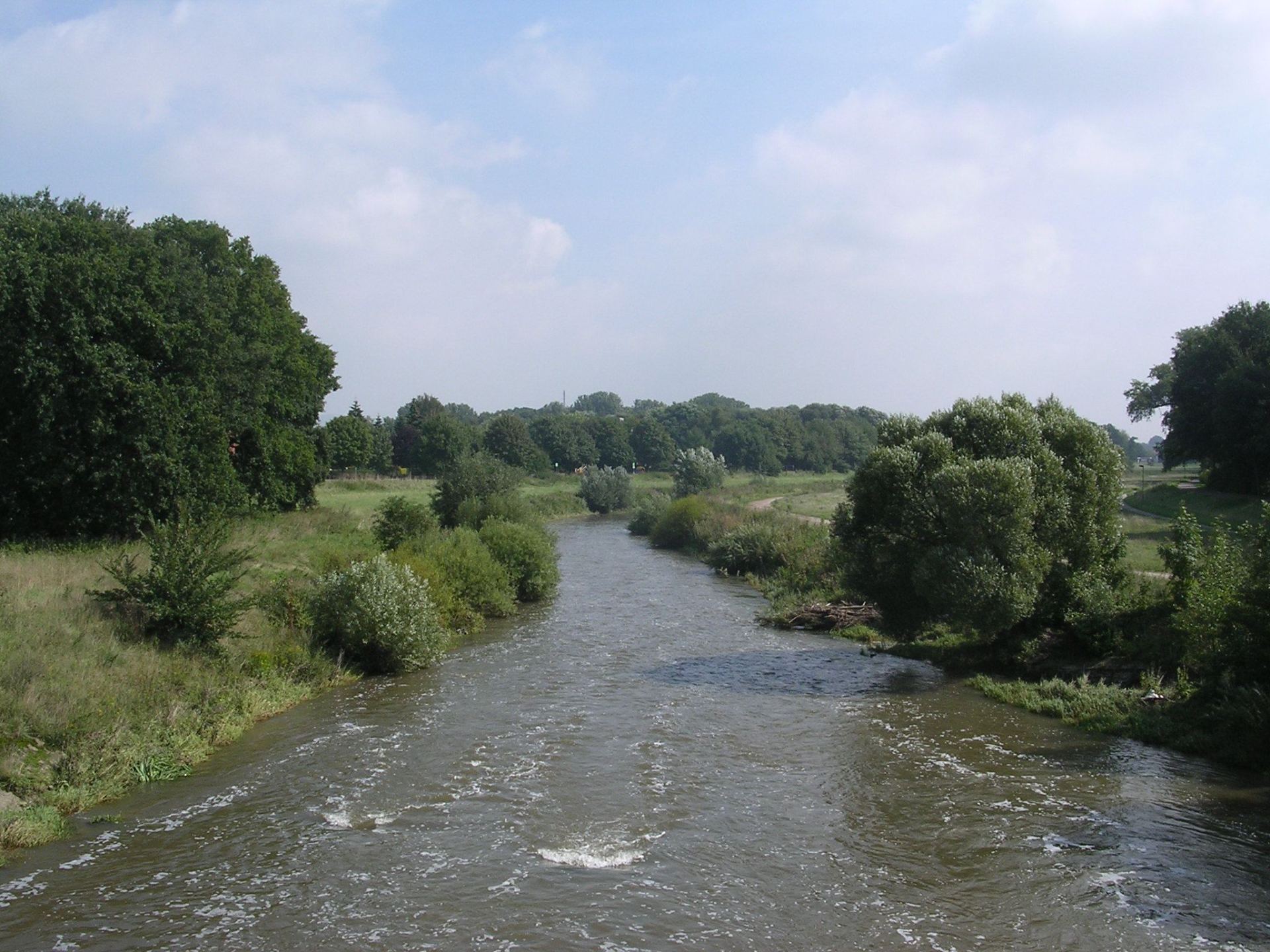 In der Mitte befindet sich ein Fluss, daneben viel Grün und ein Fuß- und Radweg 