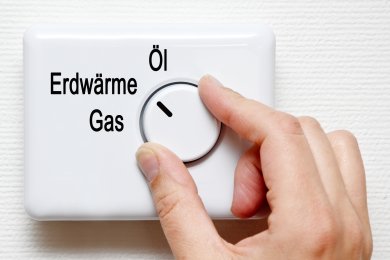 Öl, Erdwärme, Gas Ein weißer Schalter mit Drehknopf, der auf die drei Beschriftungen Öl, Erdwärme, Gas zeigen kann. Eine Hand ist zu erkennen, die den Schalter auf Erdwärme zeigen lässt.
