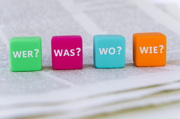 Vier verschiedenfarbige Würfel mit den Fragen "Wer?", "Was?", "Wo?" und "Wie?"