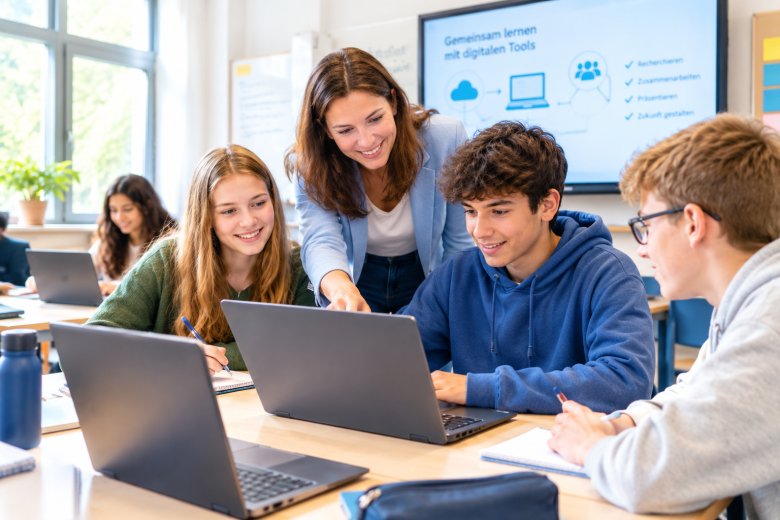 Schul-IT Eine Lehrerin und eine Gruppe Schüler*innen arbeitet im Klassenzimmer mit Notebooks.